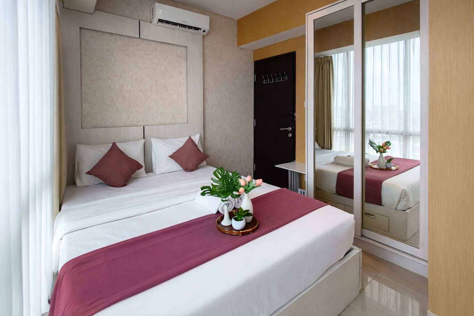 A hotel room with a bed, a mirror, a window, and an air conditioning unit.
