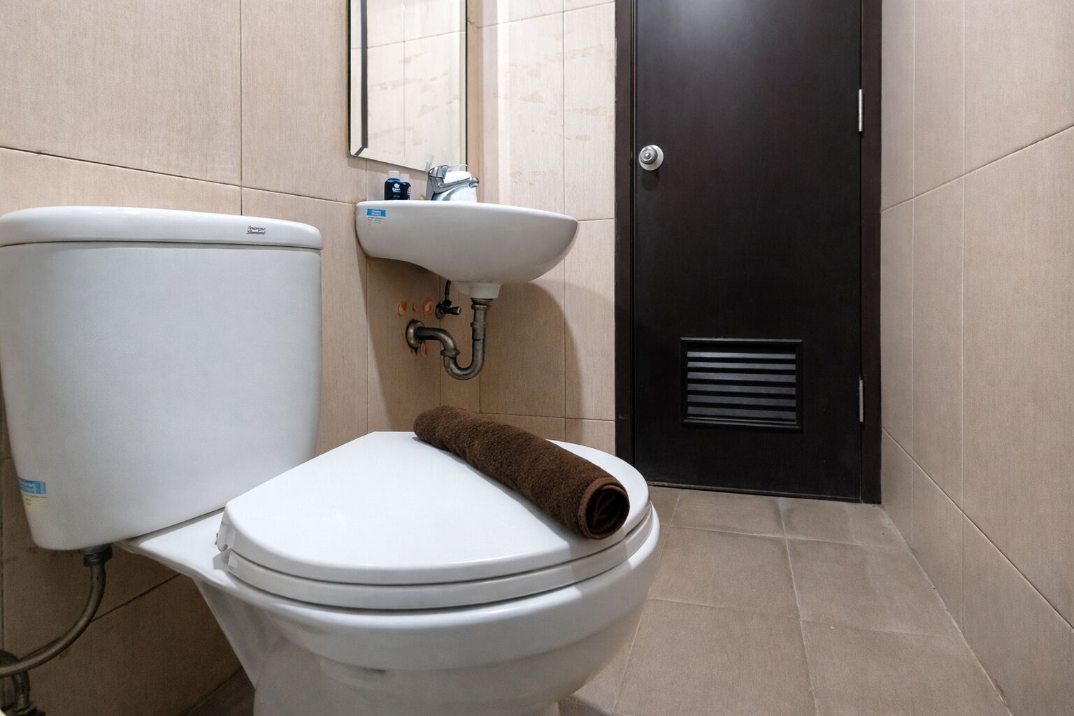A white toilet with a brown towel, a sink, and a mirror above it.