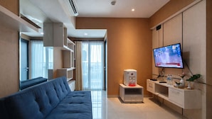 A modern living room with a sofa, a coffee machine, a TV, and a small plant. - Neat 2Br For 3 Pax At Tamansari Papilio Apartment (Surabaya)