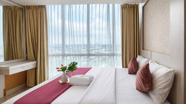 A hotel room with a bed, a desk, and a view of the cityscape. - Neat 2Br For 3 Pax At Tamansari Papilio Apartment (Surabaya)