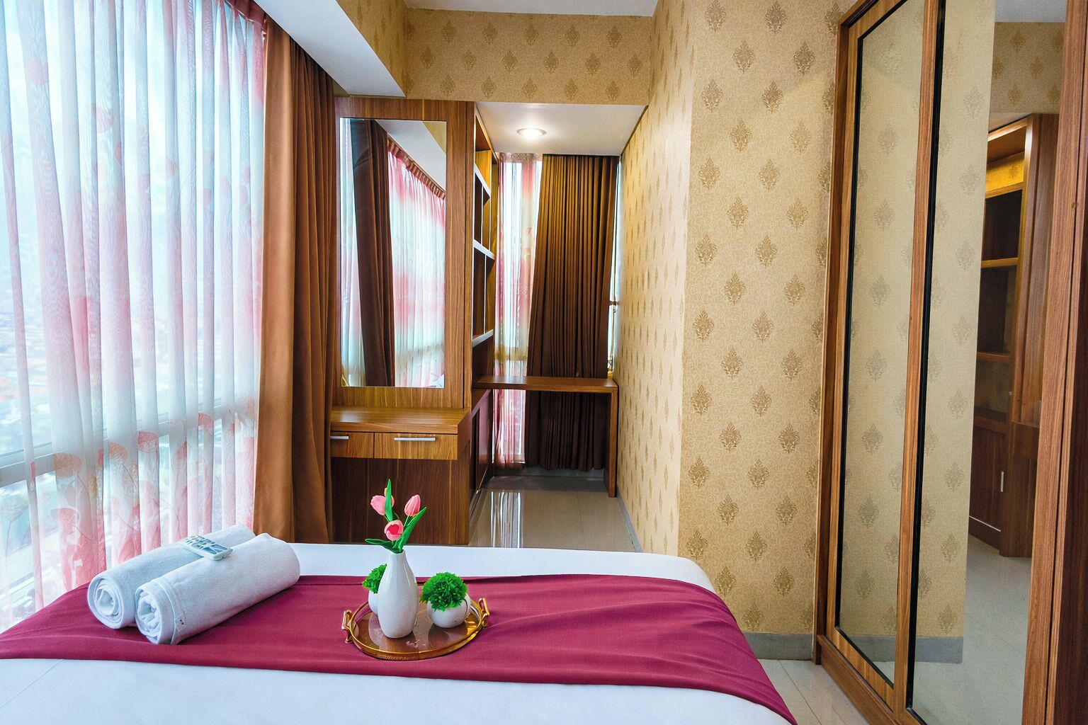 A hotel room with a bed, a mirror, a wooden wardrobe, and a bathroom visible through a door.