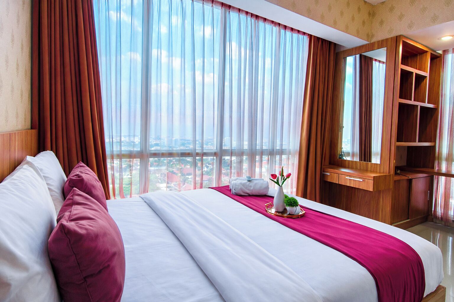 A hotel room with a large bed, a wooden wardrobe, and a view of the city.