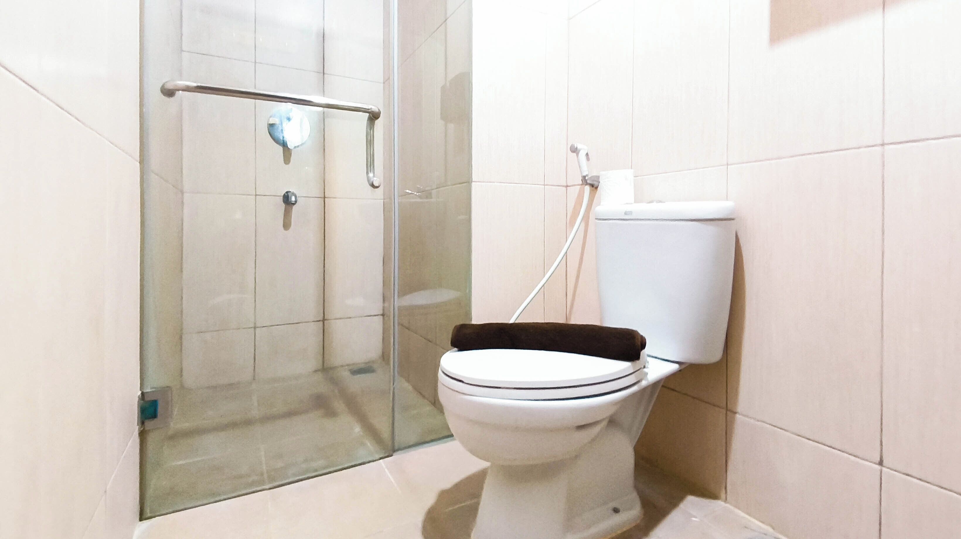 Un baño con inodoro, cabina de ducha de vidrio y barra de apoyo.