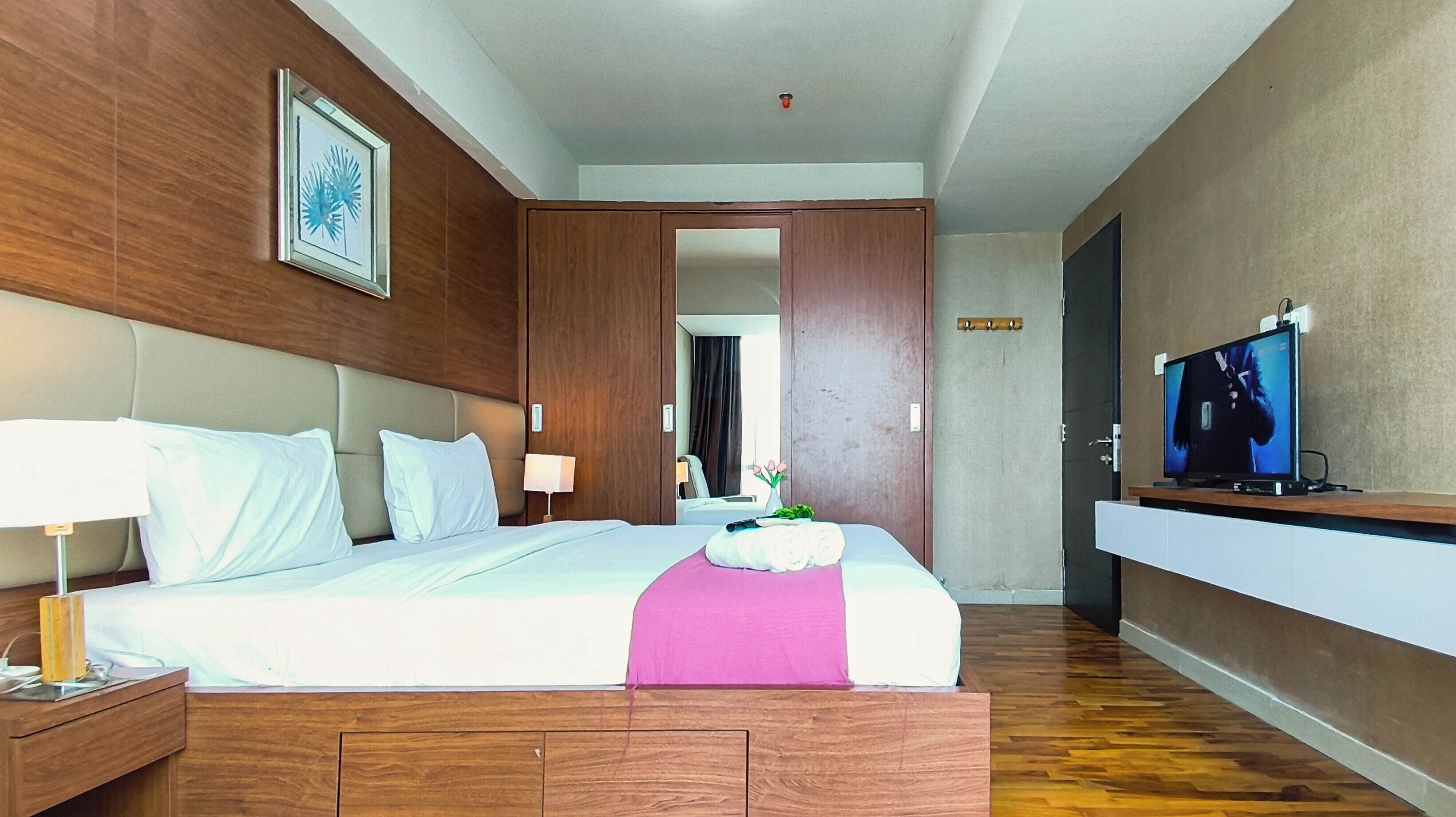 A hotel room with a bed, bedside tables, a TV, and a wooden headboard.