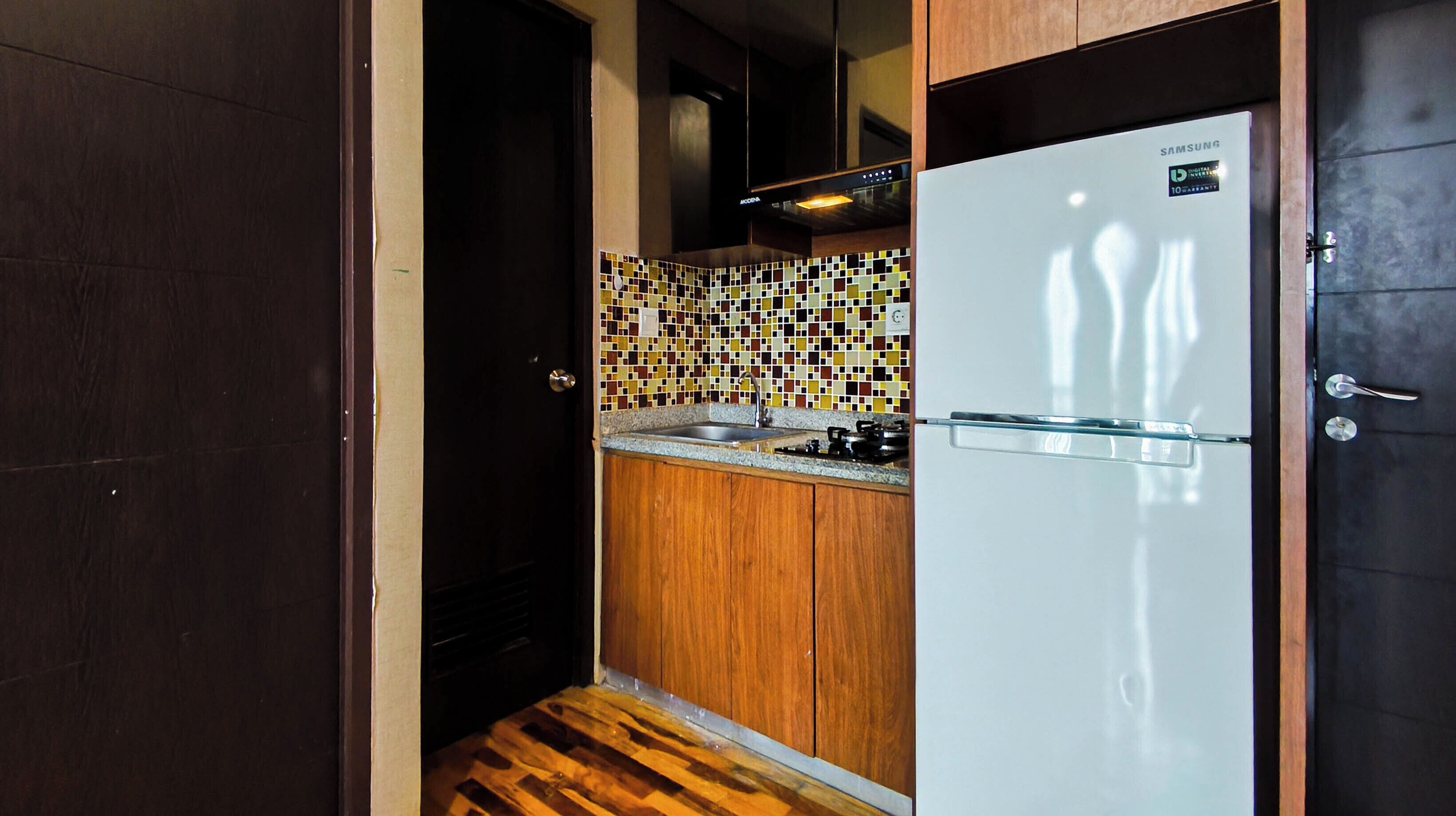A compact kitchen with a refrigerator, a sink, and a tiled backsplash.