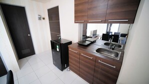 A compact kitchen with a refrigerator, a microwave, a sink, and wooden cabinets. - Cozy Stay 2Br At Tamansari Prospero Sidoarjo Apartment (Sidoarjo)