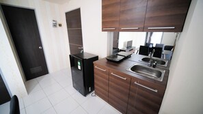 A compact kitchen with a refrigerator, a microwave, a sink, and wooden cabinets. - Cozy Stay 2Br At Tamansari Prospero Sidoarjo Apartment (Sidoarjo)