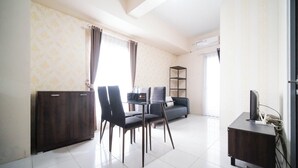 A modern living room with a sofa, dining table, chairs, a TV, and a cabinet. - Cozy Stay 2Br At Tamansari Prospero Sidoarjo Apartment (Sidoarjo)