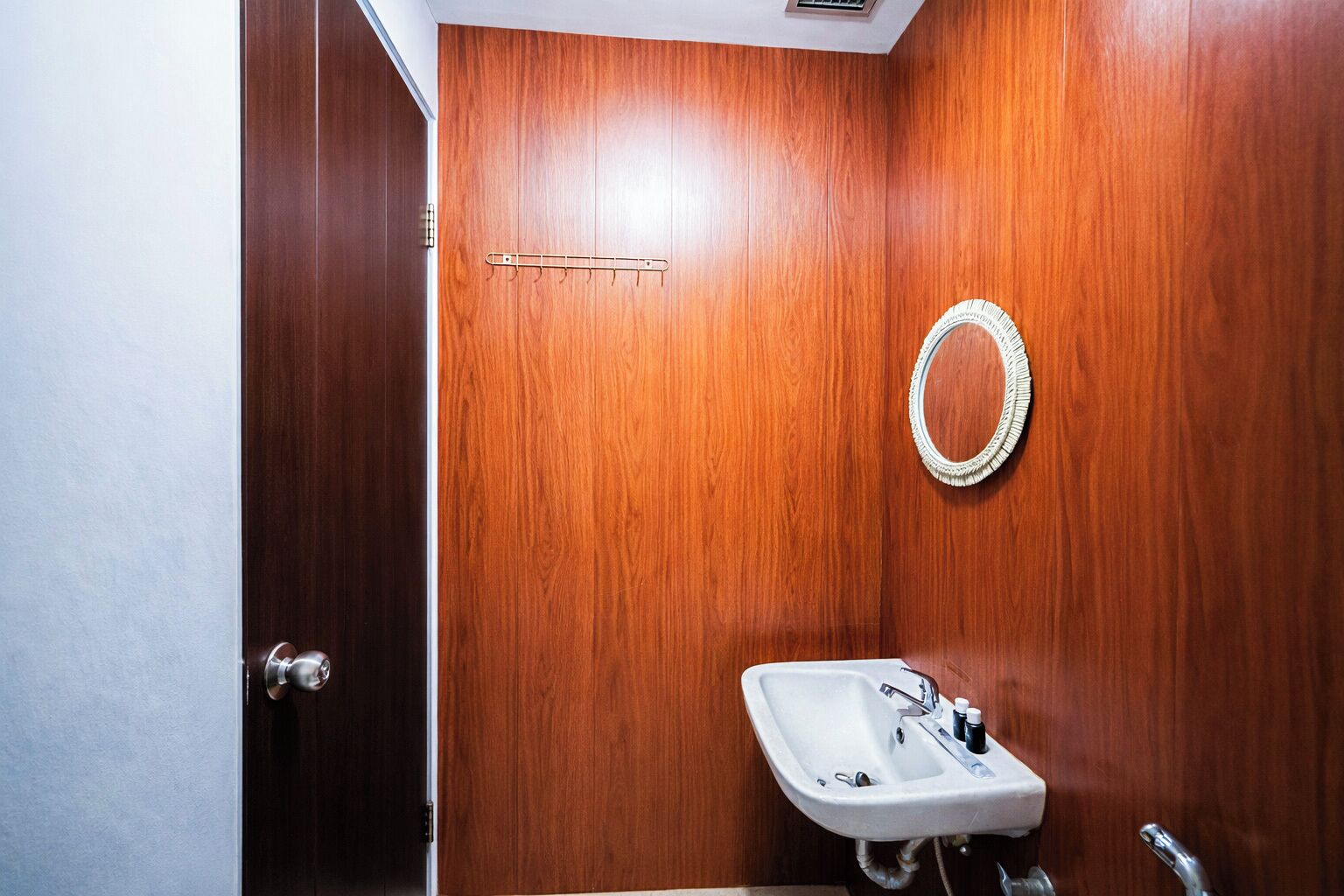 A bathroom with a wooden wall, a white sink with a mirror, and a towel rack.