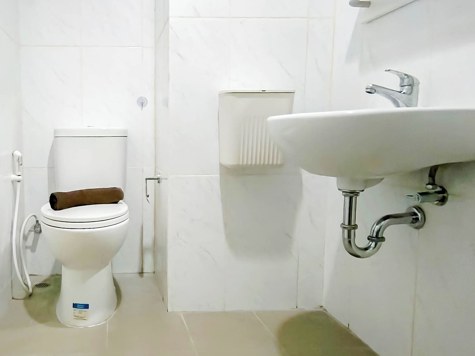 Une salle de bain équipée de toilettes, d’un lavabo fixé au mur et d’un porte-serviettes.