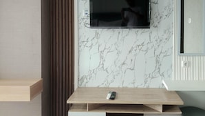 Un soggiorno moderno con una TV a schermo piatto montata su una parete in marmo, un mobile basso in legno e un piccolo telecomando sopra il mobile.