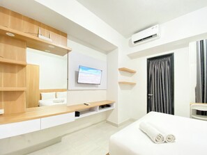 A hotel room with a bed, a TV mounted on the wall, a wooden vanity, and a door with curtains. - Best Deal Corner Studio Apartment At The Alton (Semarang)