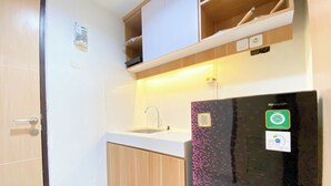 A compact kitchen with a sink, wooden cabinets, and a black refrigerator with a Sharp logo. - Best Deal Corner Studio Apartment At The Alton (Semarang)
