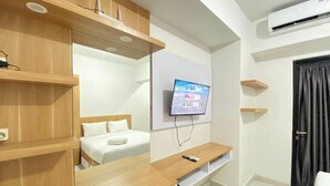 A modern hotel room with a bed, a TV mounted on the wall, a wooden console table, and a black curtain. - Best Deal Corner Studio Apartment At The Alton (Semarang)