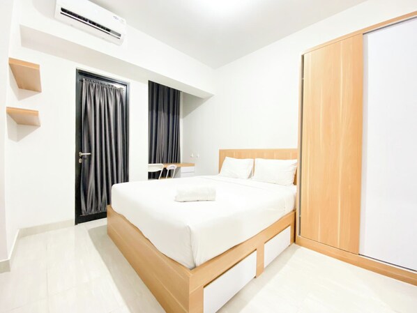 A modern hotel room with a wooden bed, a desk, a wardrobe, and an air conditioning unit. - Best Deal Corner Studio Apartment At The Alton (Semarang)