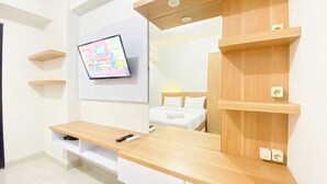 Ein modernes Hotelzimmer mit einem Holztischchen, einem wandmontierten Fernseher und integrierten Regalen.