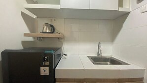 Une cuisine compacte dotée d’un évier encastré, d’un réfrigérateur noir et d’une étagère au-dessus du plan de travail.