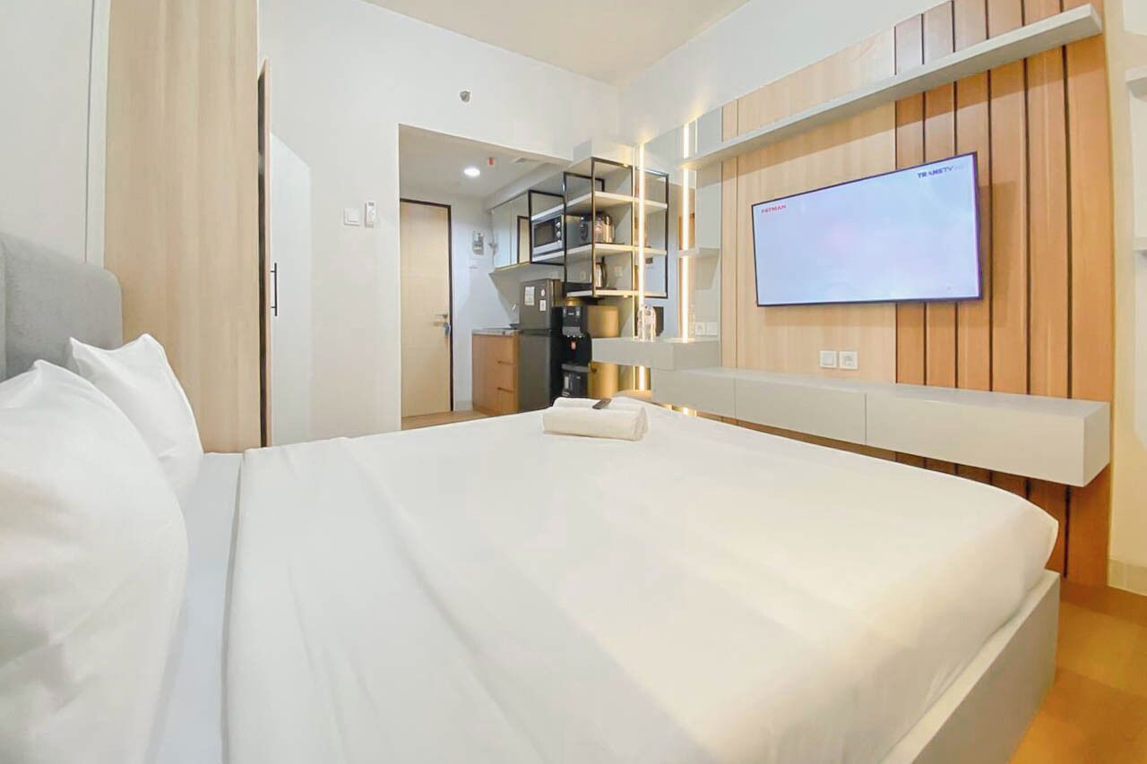 Ein Hotelzimmer mit einem Bett, einem an der Wand befestigten Fernseher, einer eingebauten Ablage und einer Tür zu einer Küchenzeile.