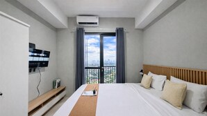 Quarto de hotel com cama, televisão, escrivaninha e janela com cortinas.