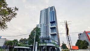 Um edifício alto e moderno com fachada de vidro curva, cercado por vegetação e céu claro.