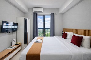 Quarto de hotel com cama, televisão na parede, guarda-roupa e janela com cortinas.