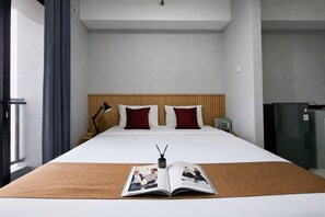Una habitación de hotel con una cama grande, una lámpara de noche, una revista y un refrigerador.