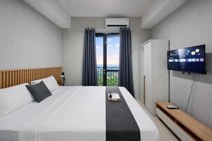 Una habitación de hotel con cama, televisor, escritorio y vistas al exterior.