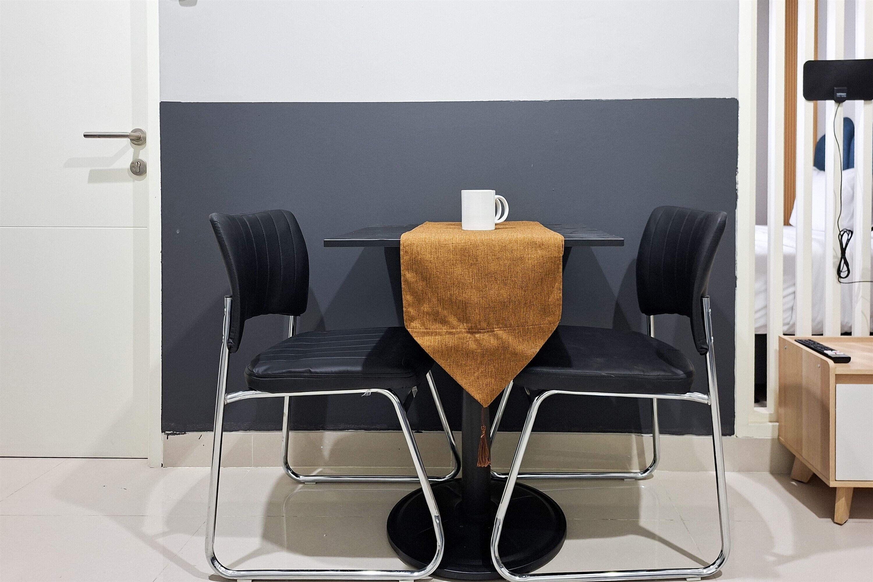 A modern room with a black and white color scheme, a round table with a white mug, two black chairs, and a wooden cabinet with a remote control.