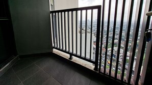 Un balcón con barandilla metálica, suelo de baldosas y vistas a un paisaje urbano.