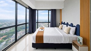 A modern hotel room with a large bed, a view of the city, and a wooden panel wall. - Homey And Spacious 3Br With City View At Apartment The Ayoma (South Tangerang)
