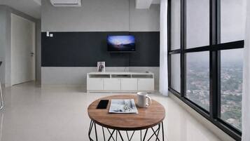 A modern room with a large window, a flat-screen TV mounted on the wall, a white cabinet, and a round table with a magazine and a mug.