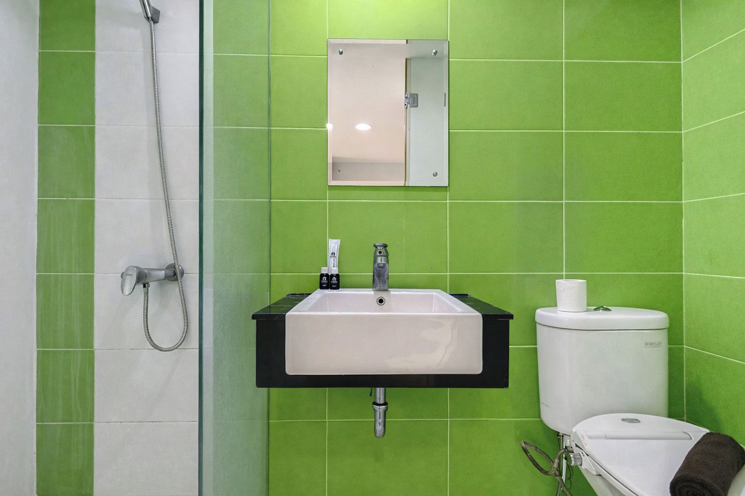 A bathroom with green tiles, a sink, a toilet, and a shower.