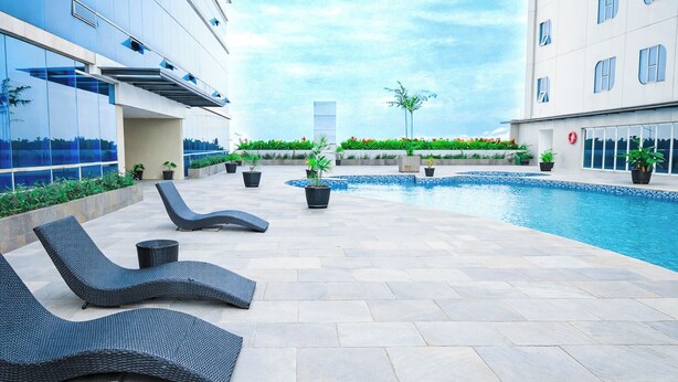 A poolside area with lounge chairs, a swimming pool, and a building with reflective glass windows. - Cozy Living Studio At The Square Surabaya Apartment (Surabaya)