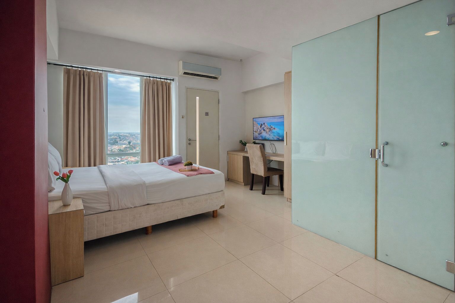 Ein Hotelzimmer mit Bett, Schreibtisch, Stuhl, Kleiderschrank und Blick auf die Stadt.