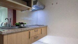 A kitchen with a granite countertop, stainless steel sink, wooden cabinets, and a white tiled backsplash. - Cozy Living Studio At The Square Surabaya Apartment (Surabaya)