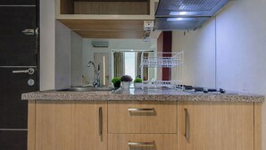 A kitchen with a granite countertop, a stainless steel sink, a dish rack, and wooden cabinets. - Cozy Living Studio At The Square Surabaya Apartment (Surabaya)