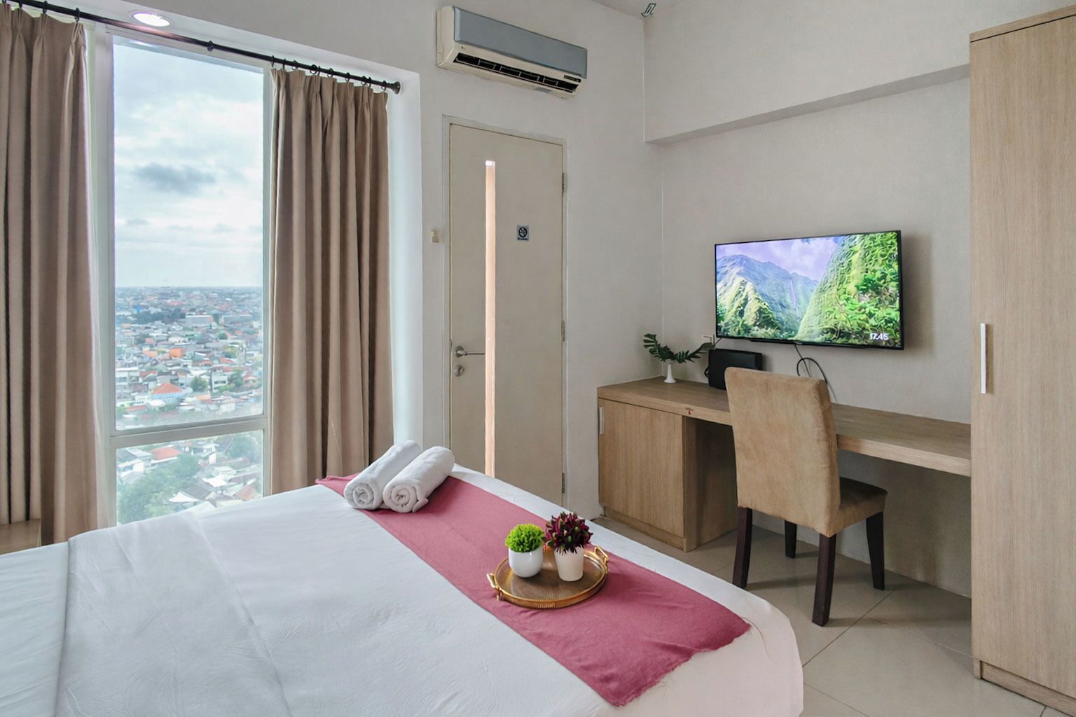 A hotel room with a bed, a desk, a television, and a view of a cityscape.