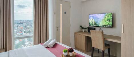 A hotel room with a bed, a desk, a television, and a view of a cityscape.