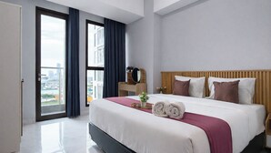 Een moderne hotelkamer met een groot bed, een houten hoofdbord, uitzicht door een schuifdeur en een stadsgezicht buiten.