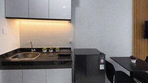 Een compacte keuken met een zwart aanrecht, een RVS spoelbak en een zwarte koelkast.