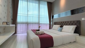 A modern hotel room with a large bed, a bedside table, a nightstand, and a window with sheer curtains. - Spacious And Lavish 4Br At The Via And The Vue Ciputra World Apartment (Surabaya)