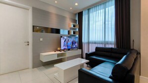 A modern living room with a flat-screen TV, a sofa, a coffee table, and a TV stand. - Spacious And Lavish 4Br At The Via And The Vue Ciputra World Apartment (Surabaya)