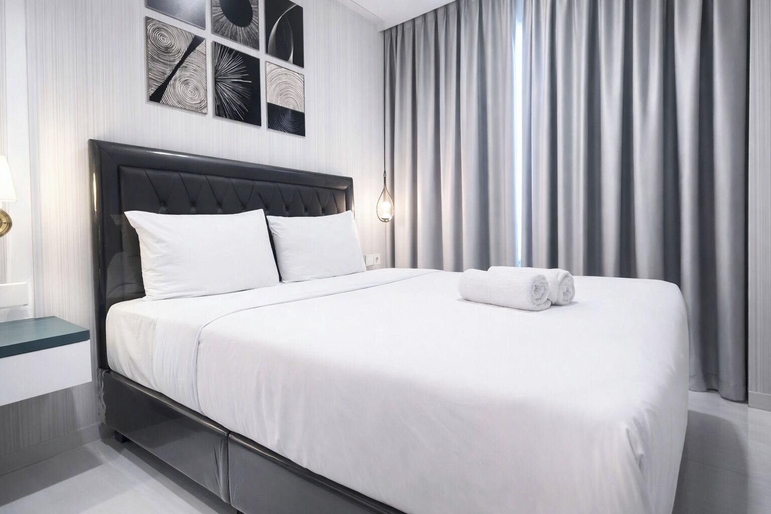 A modern hotel room with a large bed, a nightstand, a wall-mounted light, and a view of the outside through sheer curtains.