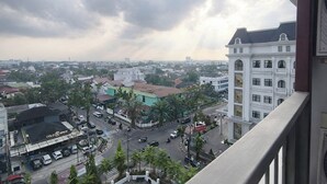 Un paisaje urbano con un edificio blanco destacado, con múltiples ventanas y balcones, un edificio con techo verde y una señal, y una calle con automóviles y un paso de peatones.