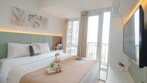 A hotel room with a bed, a TV, a balcony, and artwork on the wall. - Warm Minimalist Studio Room At Tokyo Riverside Pik 2 Apartment (Teluknaga)