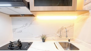 A modern kitchen with a gas stove, stainless steel sink, and marble backsplash. - Warm Minimalist Studio Room At Tokyo Riverside Pik 2 Apartment (Teluknaga)