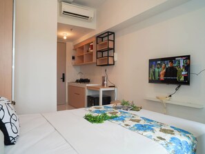 Un dormitorio con cama, televisor montado en la pared, una kitchenette pequeña y un equipo de aire acondicionado.