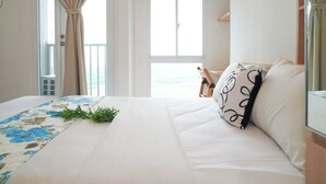 A hotel room with a bed, a view of the sea through the window, and a balcony with a chair. - Compact And Contemporary Studio Apartment Tokyo Riverside Pik 2 (Teluknaga)