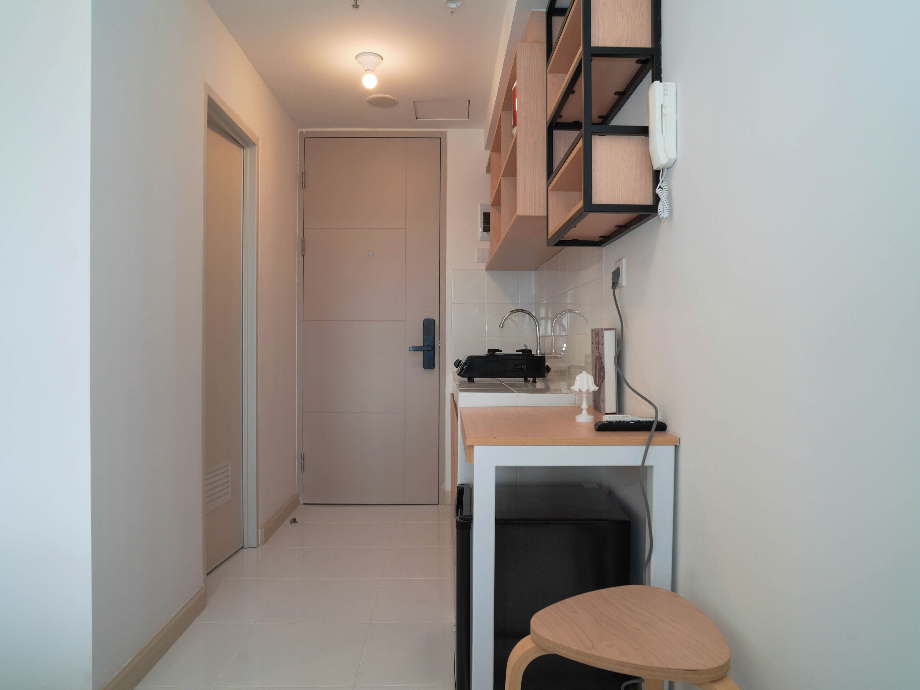A narrow hallway with a door at the end, a small kitchenette with a sink and a countertop, and a chair.