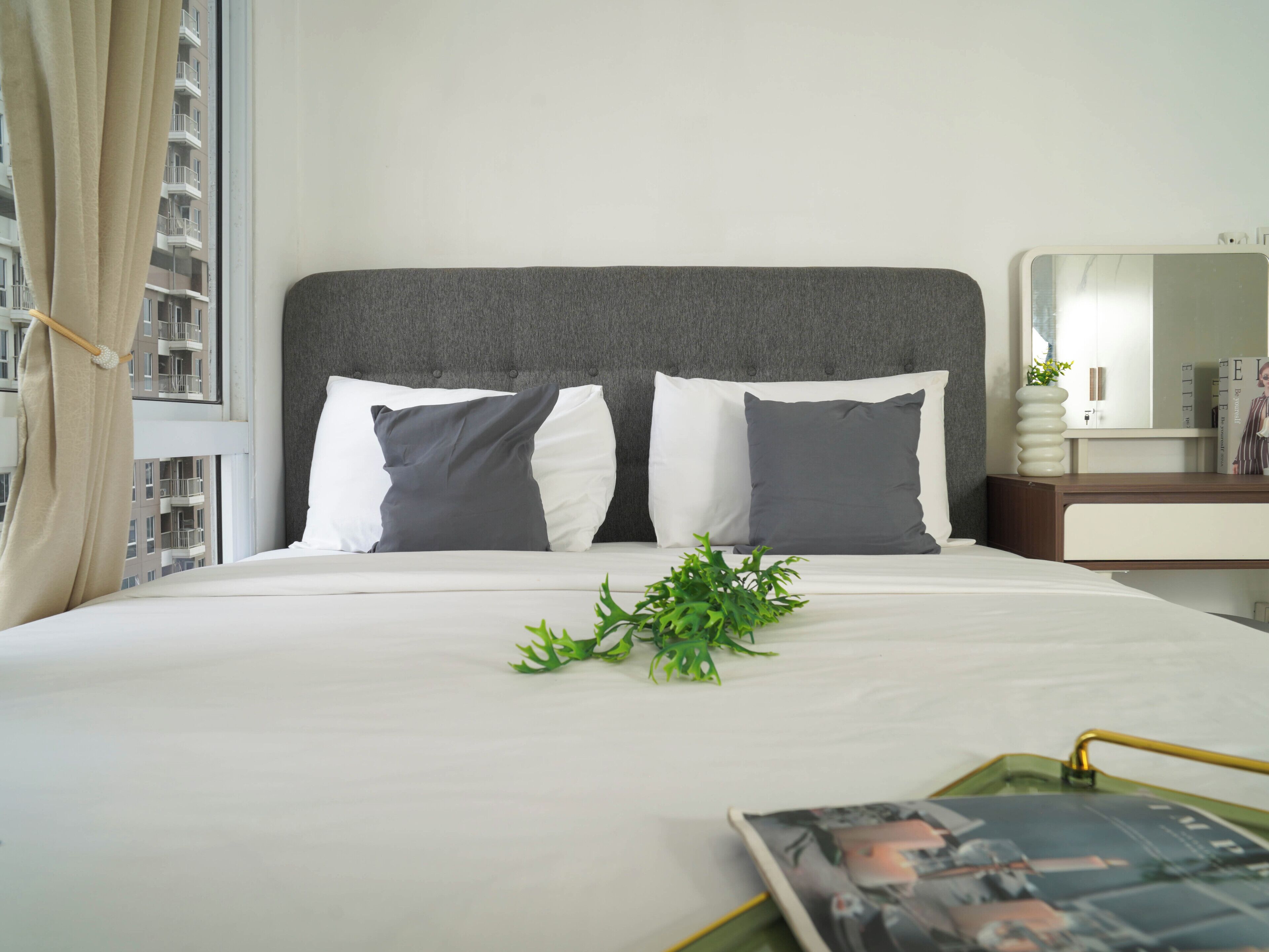 A neatly made bed with two pillows, a bedside plant, and a magazine on the nightstand.